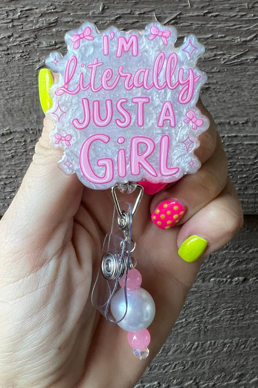 Hand holding a badge reel with 'I'm literally just a girl' text with pearl background and coordinating badge bling.