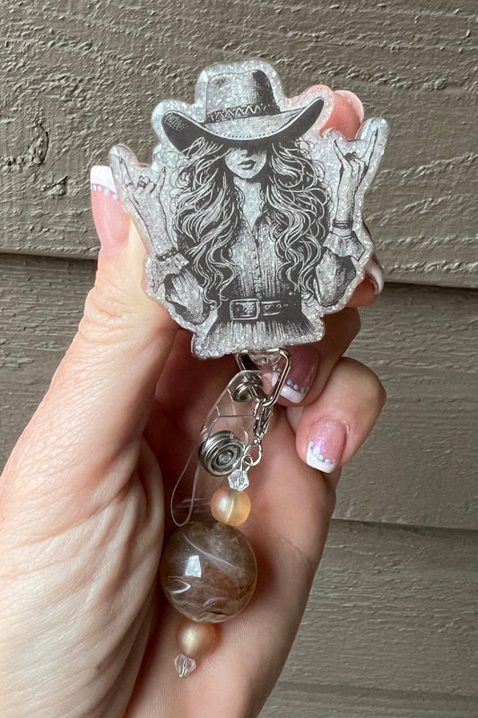 A monochrome badge reel showing a long-haired cowgirl in a hat throwing rock-on hand signs, with coordinating badge bling.