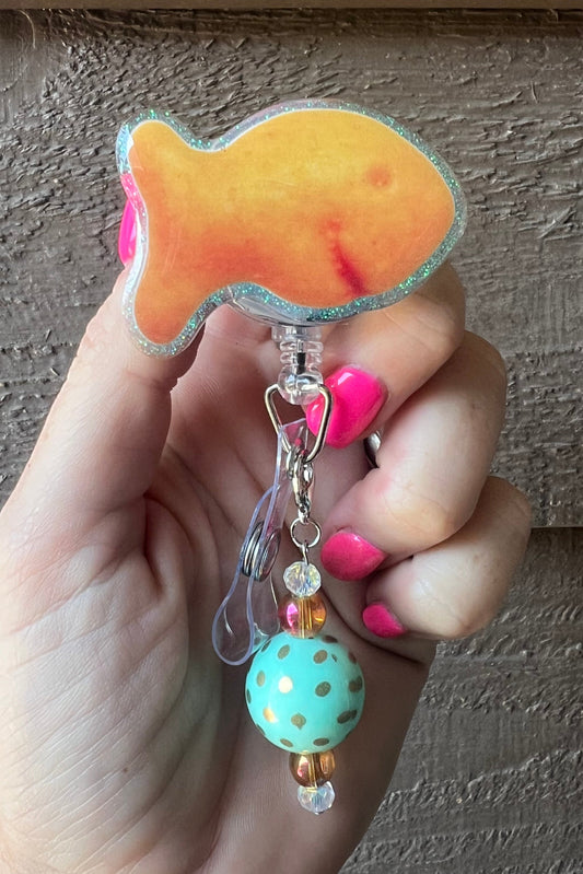Goldfish cracker shaped badge reel with aqua glitter border and mint dangle.
