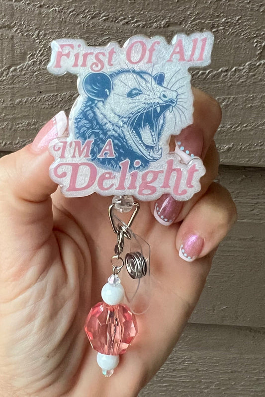 Funny Opossum Badge Reel with "First of all I'm a Delight" over pearl color with added peach badge bling.