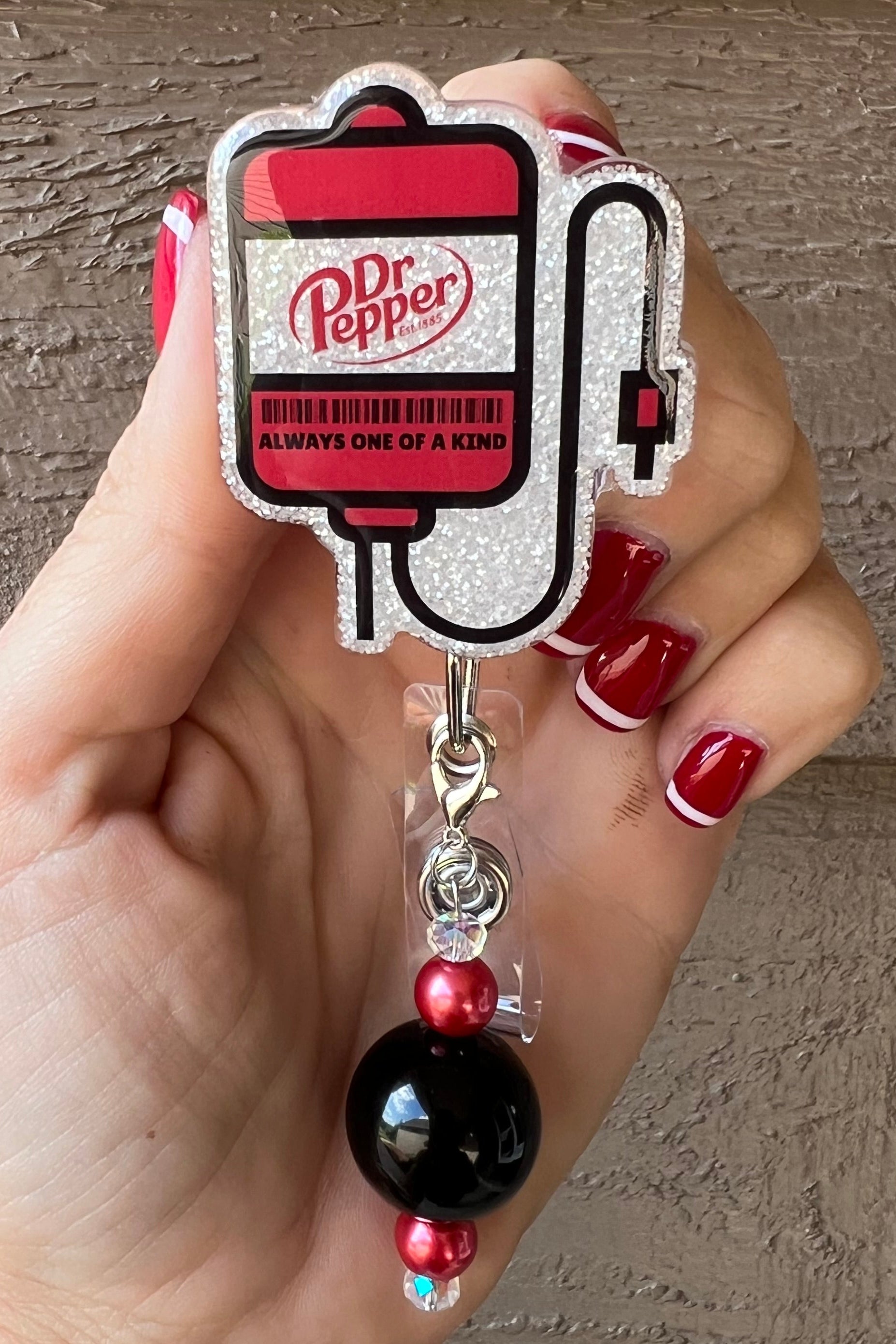 Dr. Pepper IV badge reel with red and black beaded dangle and "Always one of a kind" text