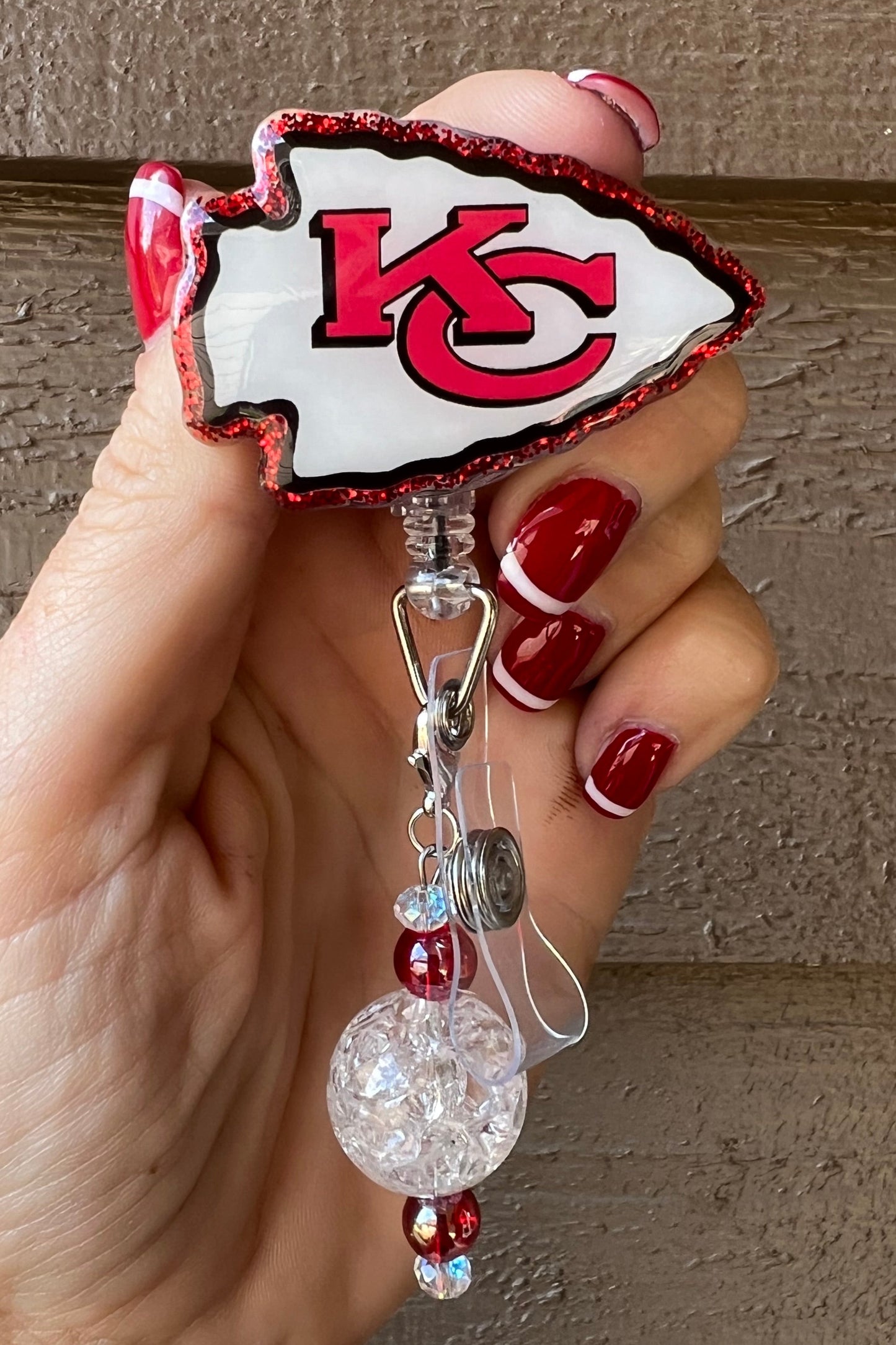 Kansas City Chiefs badge reel outlined in red glitter with a white and red beaded dangle.