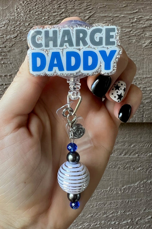 Hand holding badge reel with the words "Charge Daddy" with silver border and  coordinating badge bling.