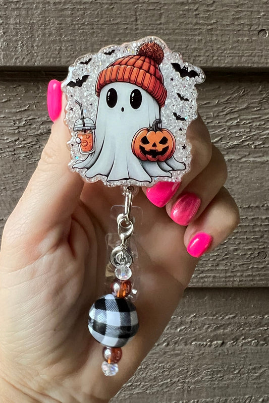 Halloween badge reel with glittery ghost in orange beanie holding a pumpkin and boba drink, with bubbalo plaid and orange beaded dangle.