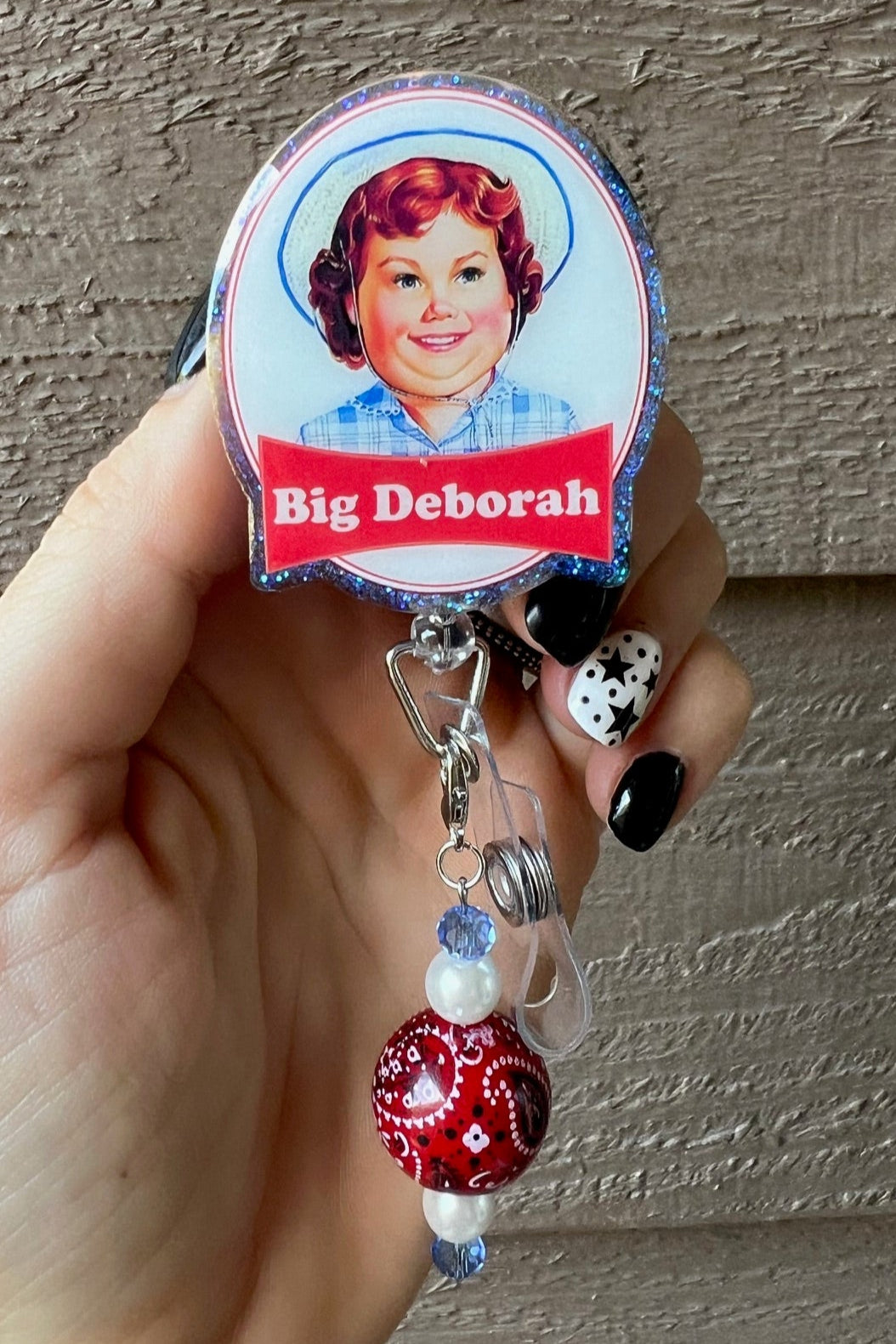 Hand holding badge reel with blue glitter border and grown up Deborah the snack cake girl.