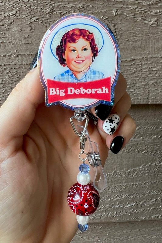 Hand holding badge reel with blue glitter border and grown up Deborah the snack cake girl.