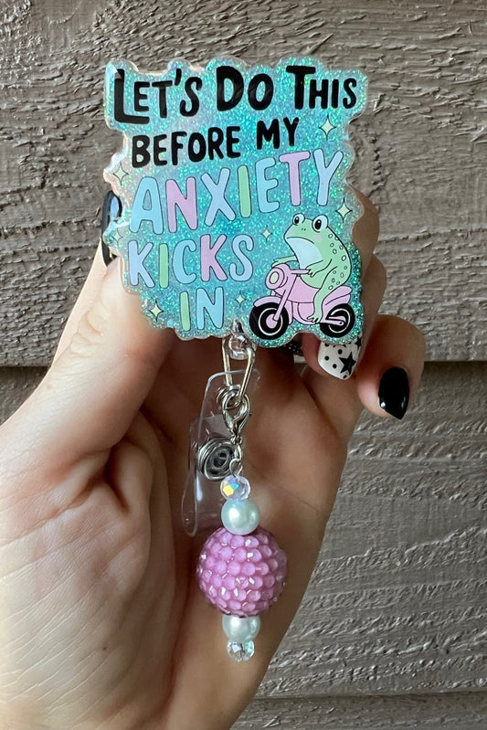 Hand holding aqua glitter badge reel with the text "Let's Do this before my Anxiety kicks in" with frog riding cycle and coordinating badge bling.