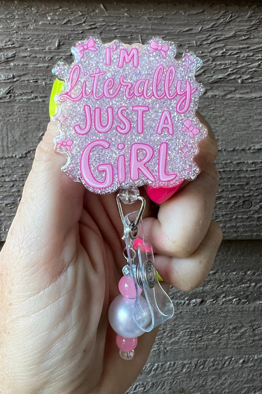 Hand holding badge reel that says "I'm Literally Just a Girl" with matching badge bling.