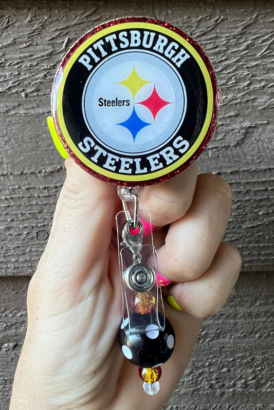 Hand holding a badge reel with Pittsburgh Steelers logo with coordinating badge bling.