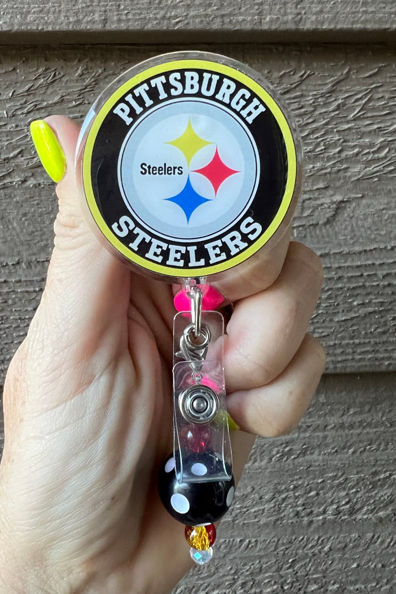Hand holding a badge reel with a Pittsburgh Steelers logo against a textured wall.