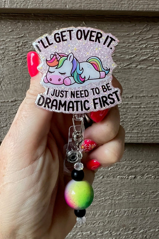 Sleepy Unicorn badge reel that says "I'll get over it. I just need to be dramatic first" on soft pink glitter background with coordinating badge bling.