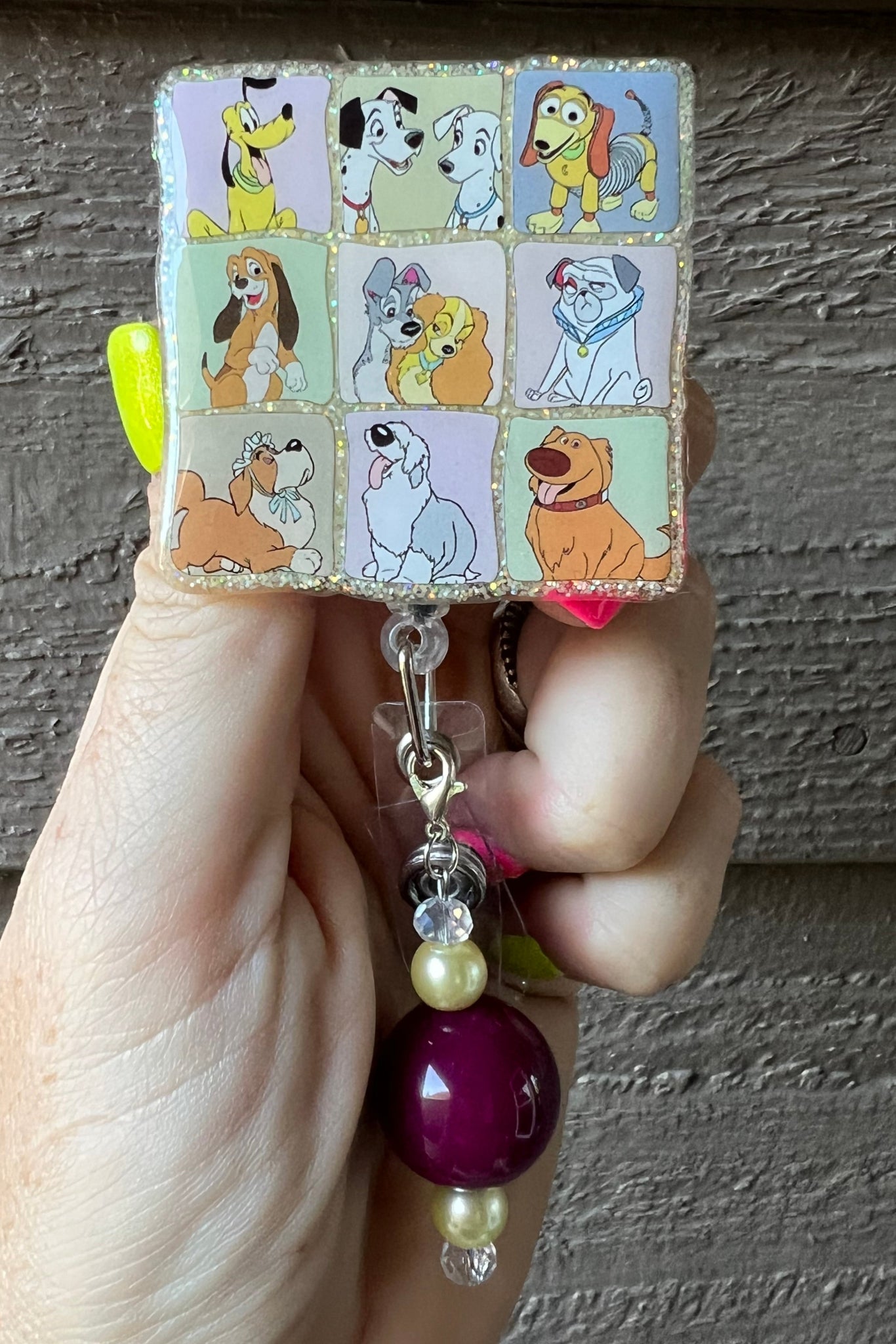 hand holding badge reel featuring 9 different squares with Disney dogs in each square and coordinating badge bling.
