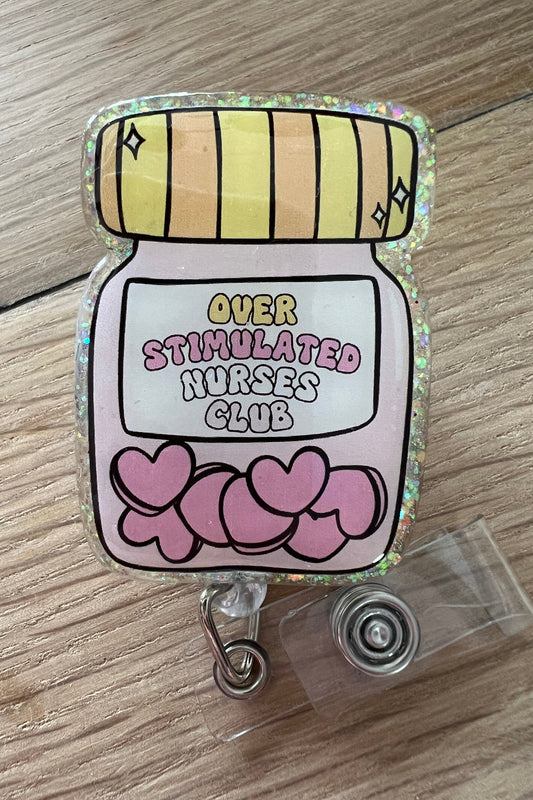 Glitter badge reel with cartoon pill jar that says “Overstimulated Nurses Club” and pink hearts inside