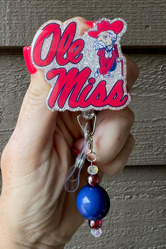 Ole Miss Badge Reel on white glitter background with coordinating badge bling.