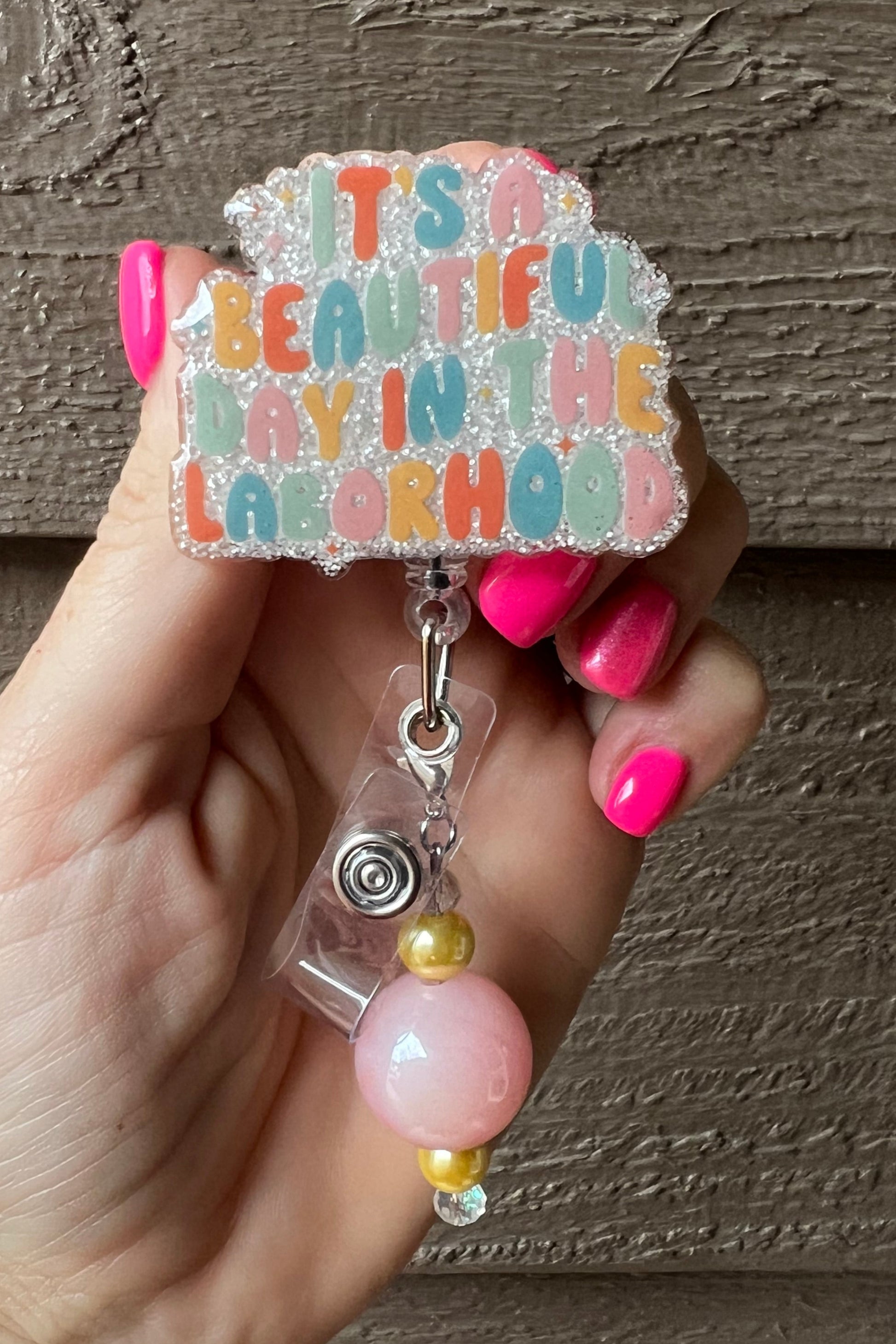 Soft Glitter Badge Reel featuring the phrase "It's a beautiful day in the laborhood" with soft pink and gold beaded dangle.