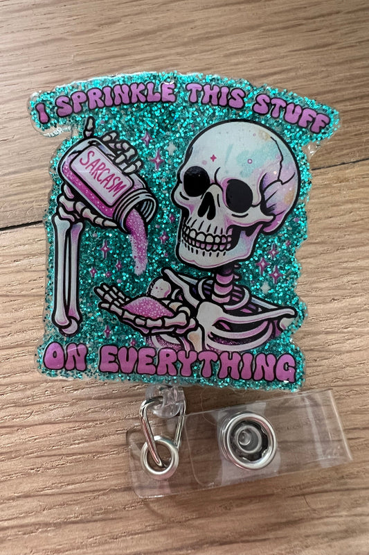 “Glittery badge reel featuring a skeleton sprinkling sarcasm from a spice jar with the phrase ‘I sprinkle this stuff on everything’ in pink text.”