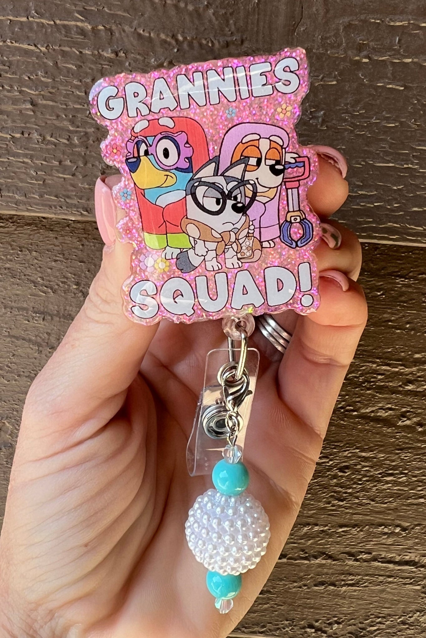 Pink glitter badge reel with cartoon dogs dressed as grannies, featuring the phrase ‘Grannies Squad’ in bold letters.