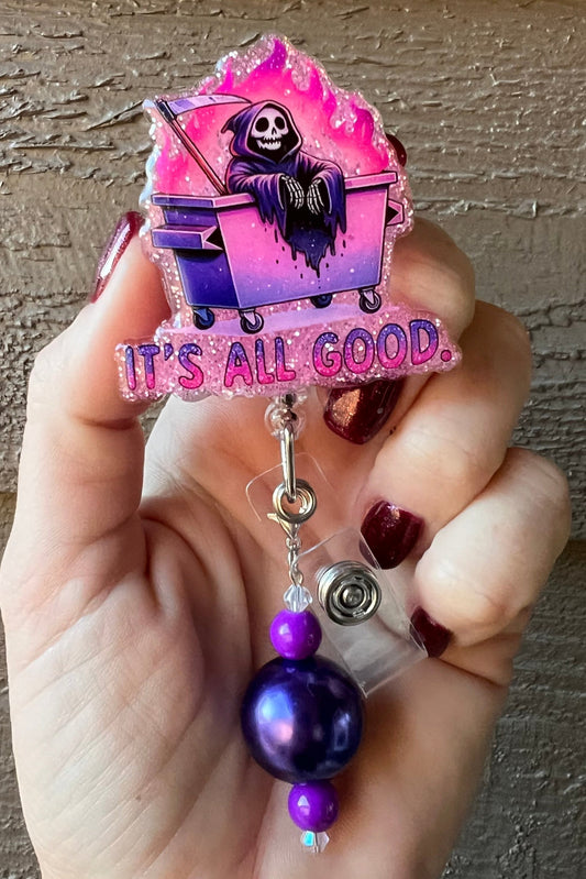 Pink Glitter Badge Reel featuring a cartoon Grim Reaper lounging in a pink and purple dumpster fire with the text "It's All Good," with coordinating badge bling.