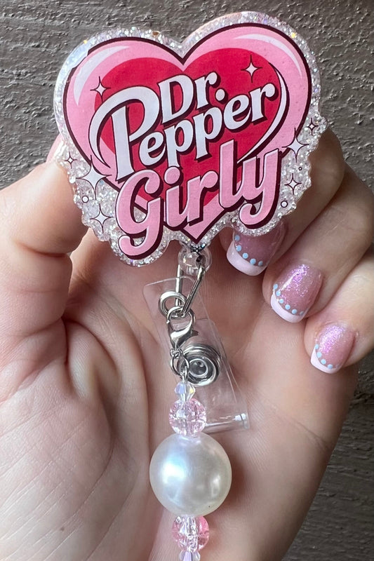Pink heart-shaped badge reel with "Dr. Pepper Girly" in retro font and glittery border.