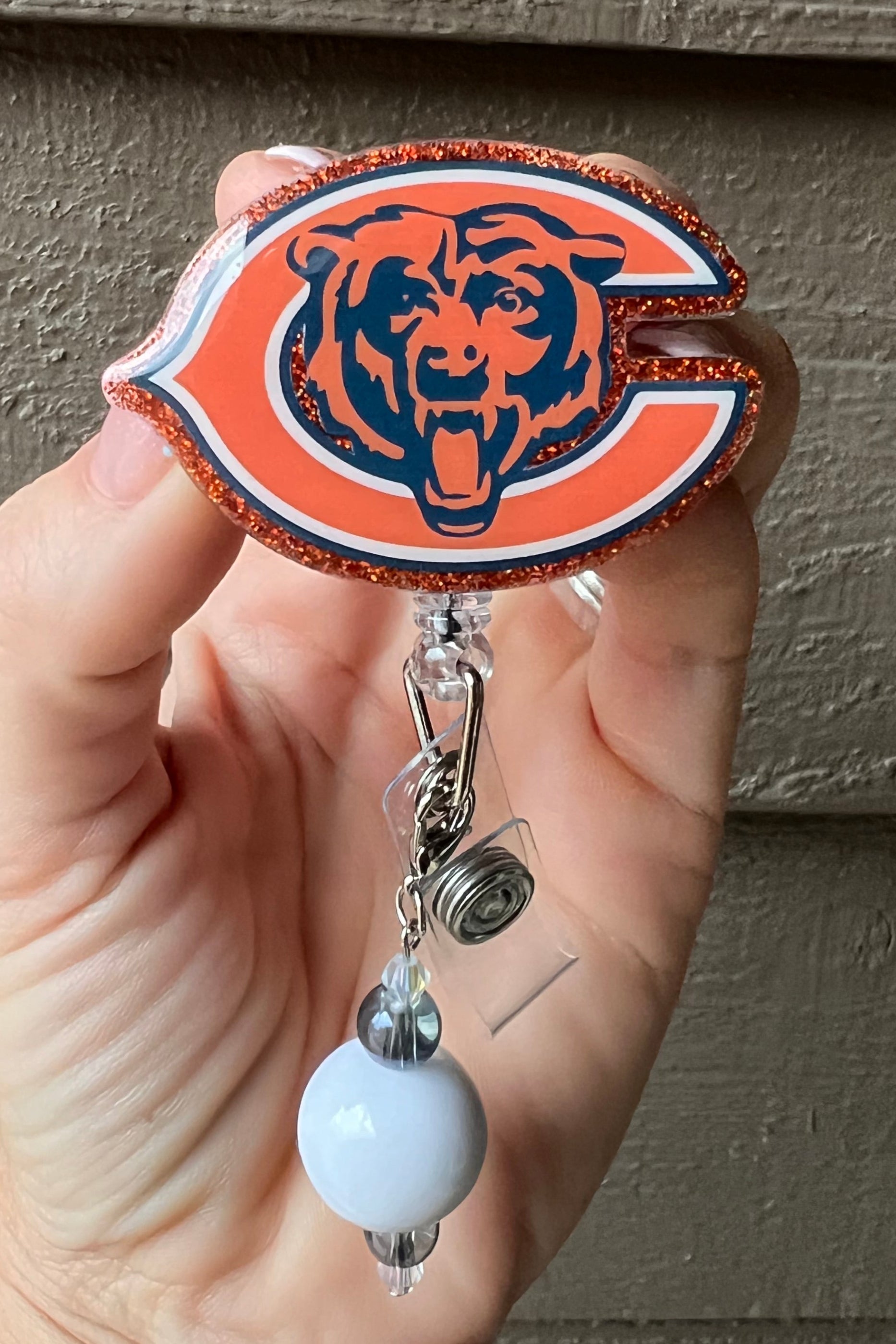 Chicago bears badge reel bordered with orange glitter and a white and navy beaded dangle