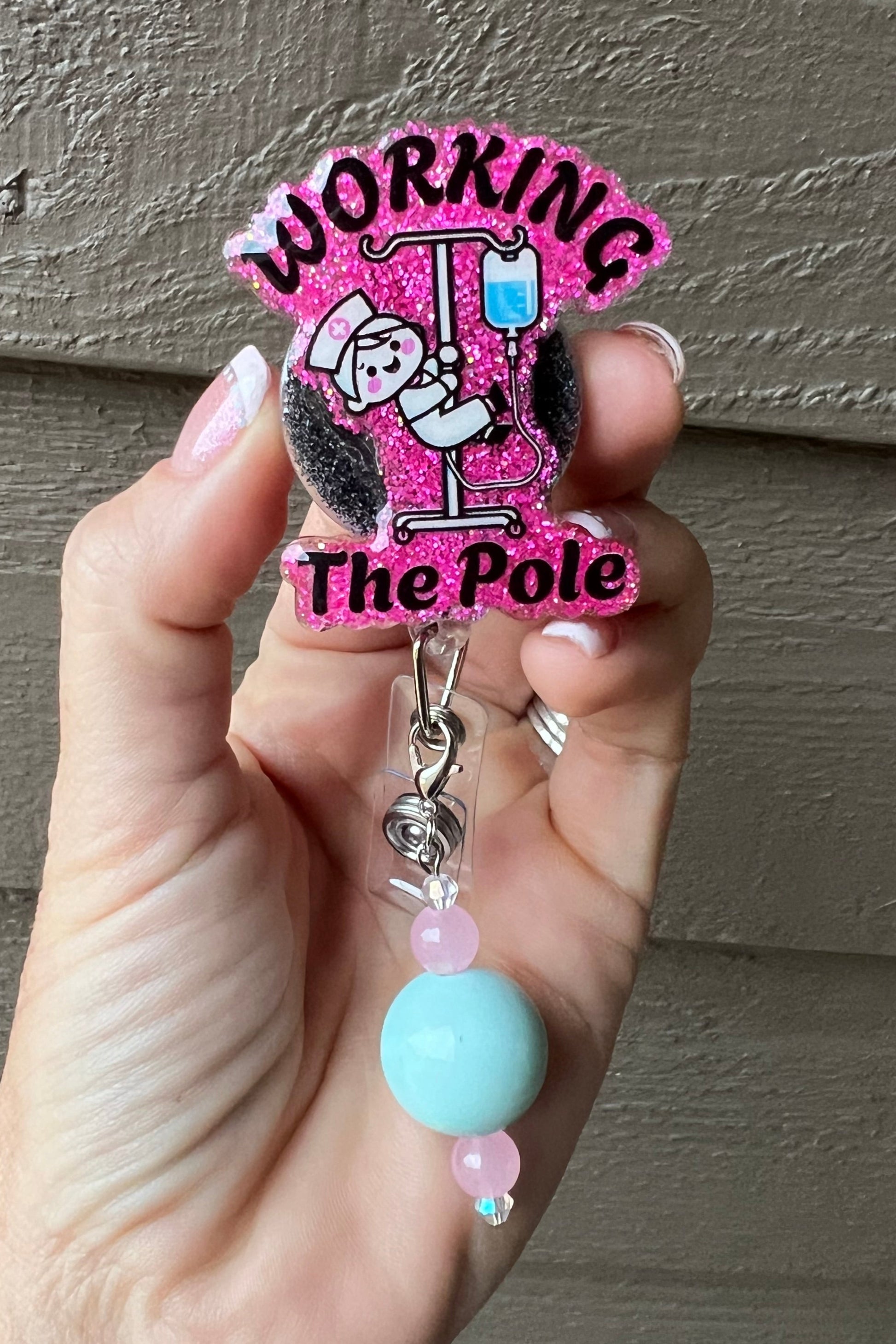 A glittery pink badge reel with a cartoon nurse pole dancing on an IV stand and the words "Working the Pole," accented with a coordinating badge bling.