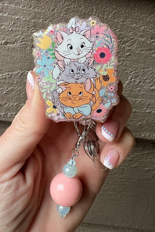 Aristocats badge reel with flora background on soft purple glitter and pink/blue beaded dangle