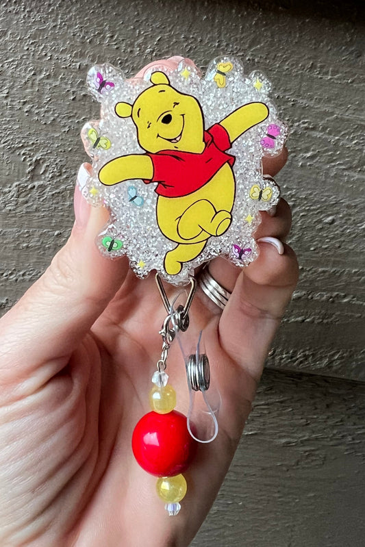 Glittery Winnie the Pooh badge reel with bees and a red and yellow beaded dangle.