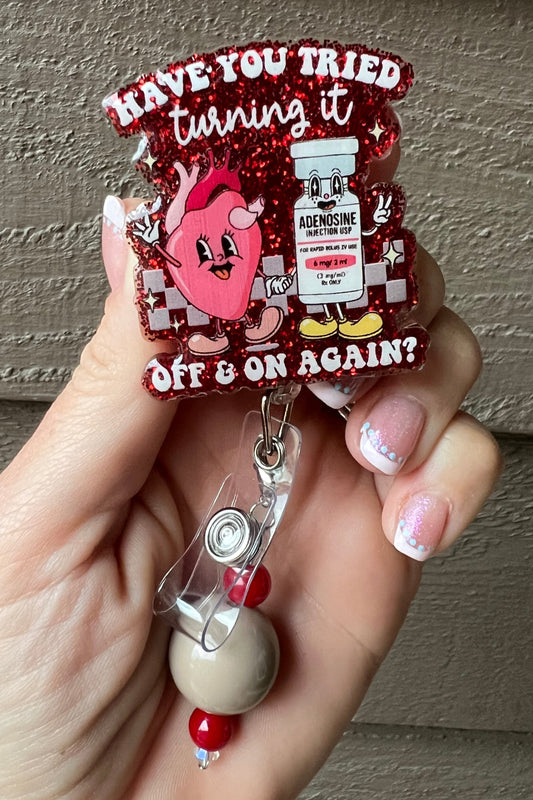 A glittery red badge reel with a cartoon heart and adenosine vial saying "Have you tried turning it off & on again?", paired with a coordinating badge bling.
