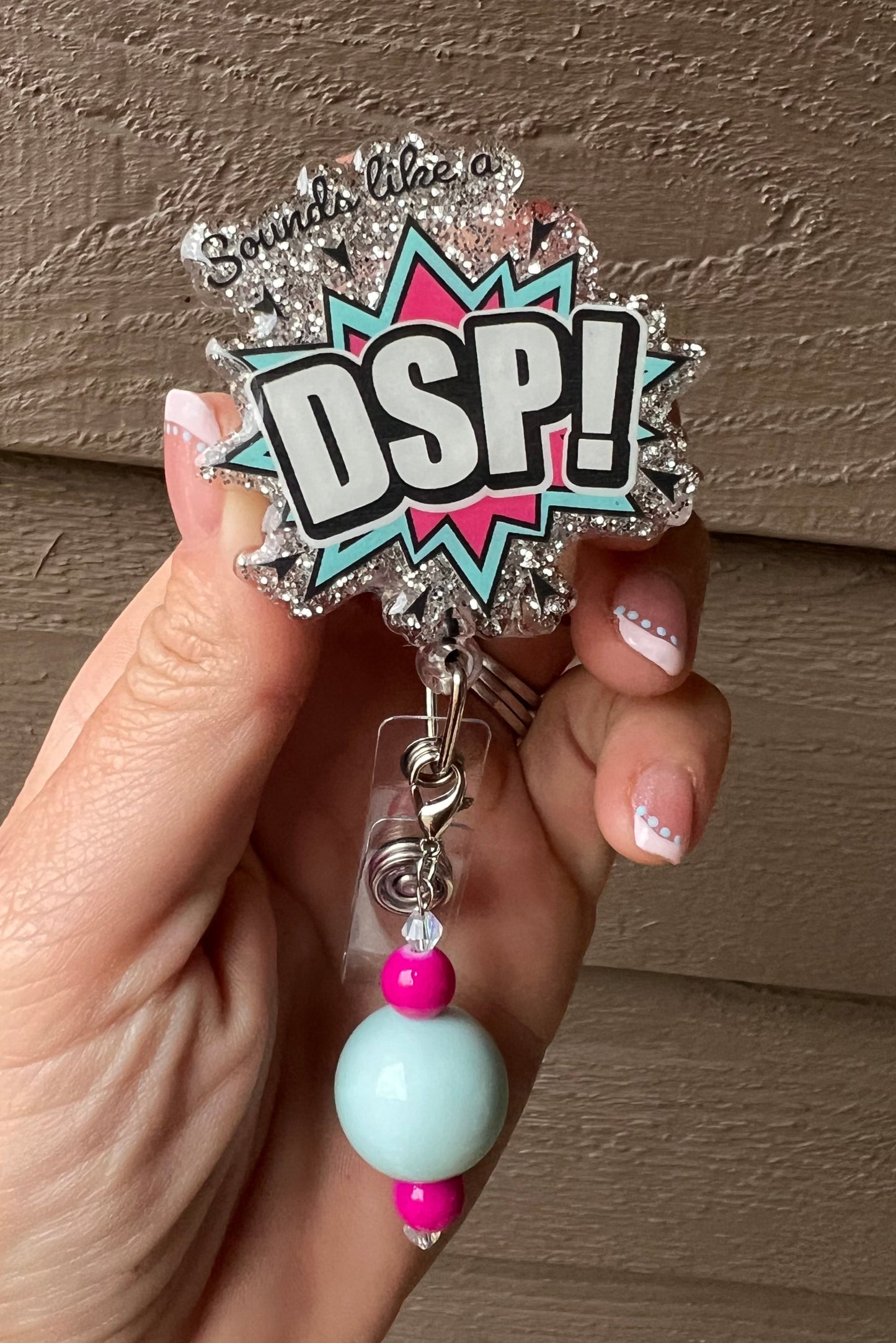 Silver Glitter Badge Reel with comic-style text reading "Sounds like a DSP!" in pastel mint and pink paired with a coordinating badge bling.