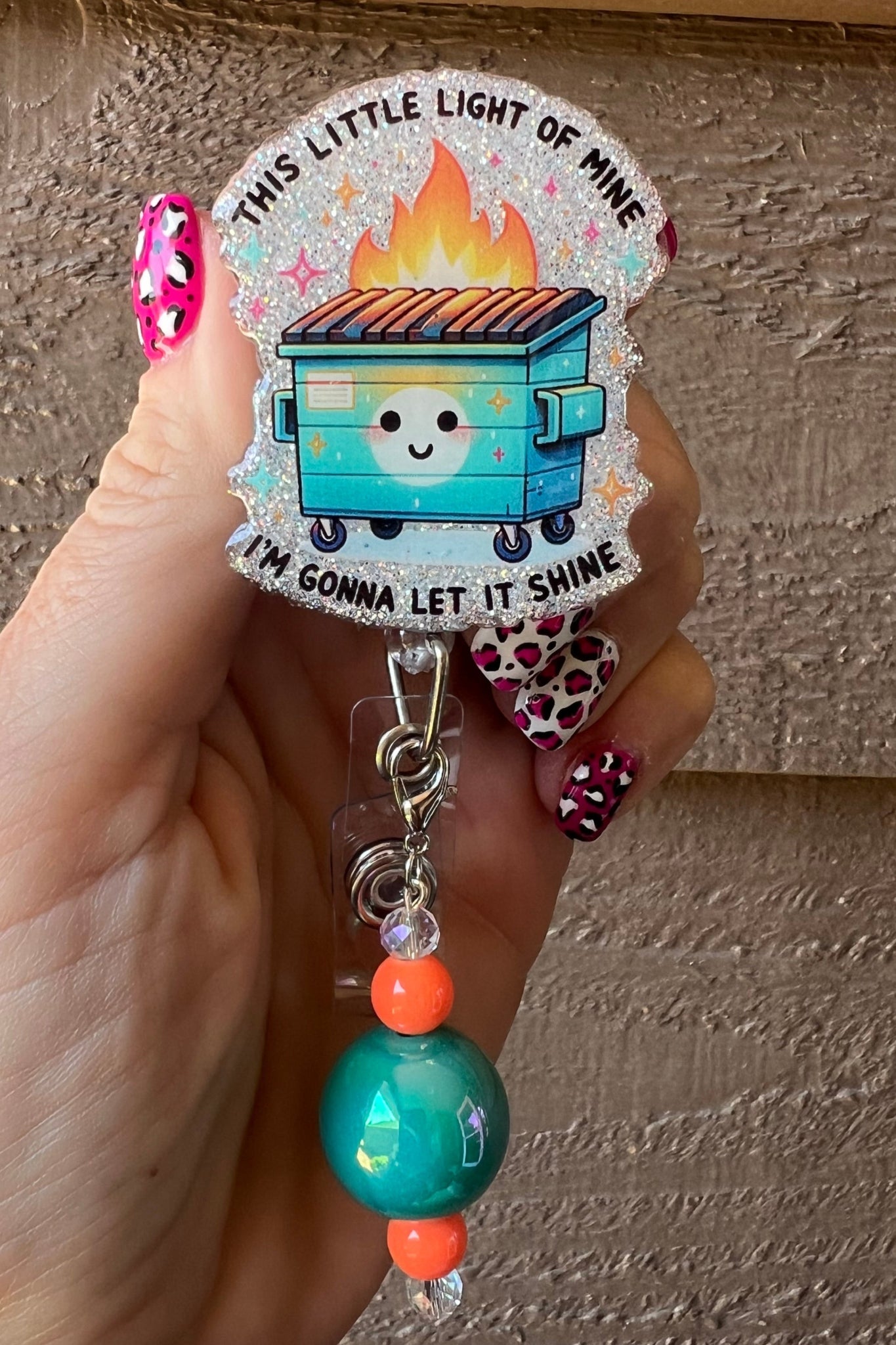 Smiling Dumpster on Fire Badge Reel with "This little light of mine i'm gonna let it shine" printed over soft blue glitter.