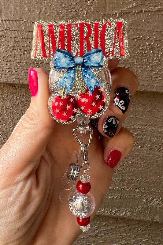 Silver "America" badge reel with red, white and blue theme and star studded cherries with blue bow.