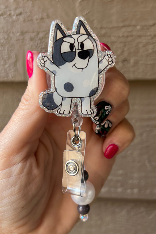 Glittery badge reel featuriing Muffin from Bluey with black, white, and pearl beaded dangle