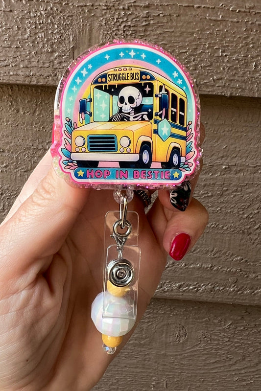 "Struggle Bus - Hop in Bestie" badge reel featuring skeleton bus driver and coordinating badge bling.