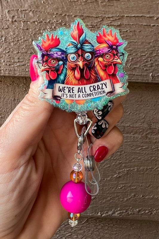 Badge reel with three silly chickens and text that reads "We're All Crazy - It's not a competition," on soft blue glitter with coordinating badge bling.