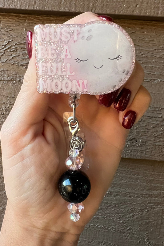 Soft pink glitter badge reel with sleeping moon and the words "must be a full moon" with coordinating badge bling.