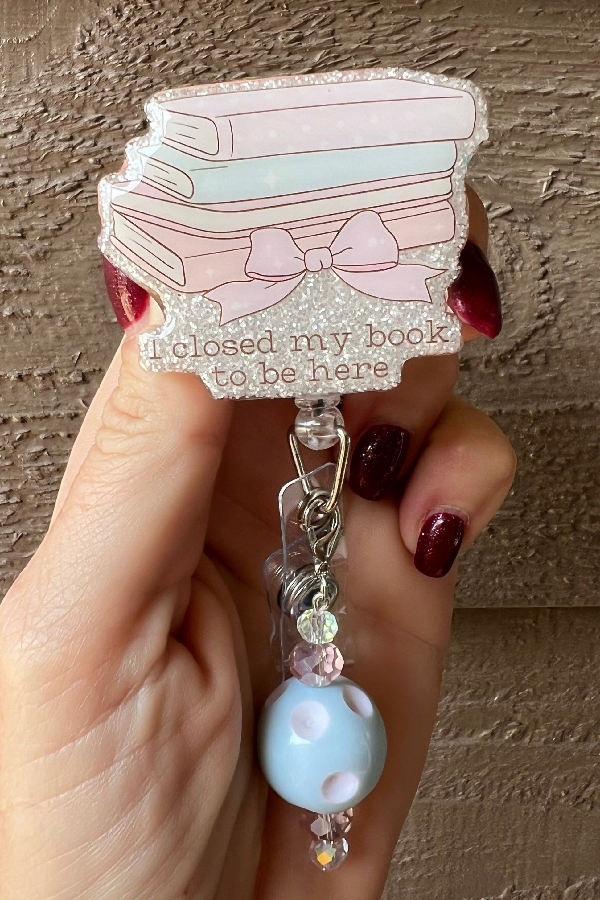 A funny badge reel featuring a pastel stack of books that reads “I closed my book to be here,” decorated with glitter. Ideal for book lovers, teachers, and librarians with a sense of humor.
