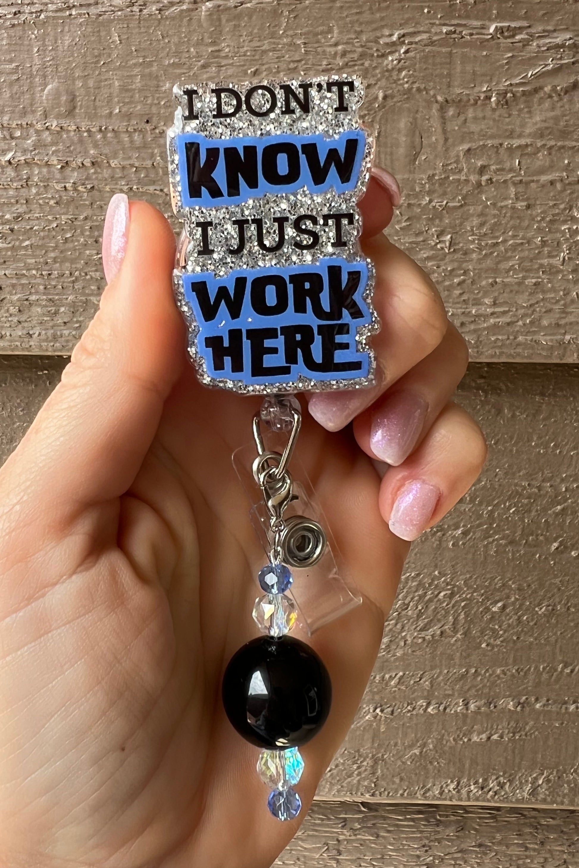 Glittery badge reel with the phrase “I Don’t Know, I Just Work Here,” paired with black and crystal beaded charm. Perfect for adding humor to work badges.