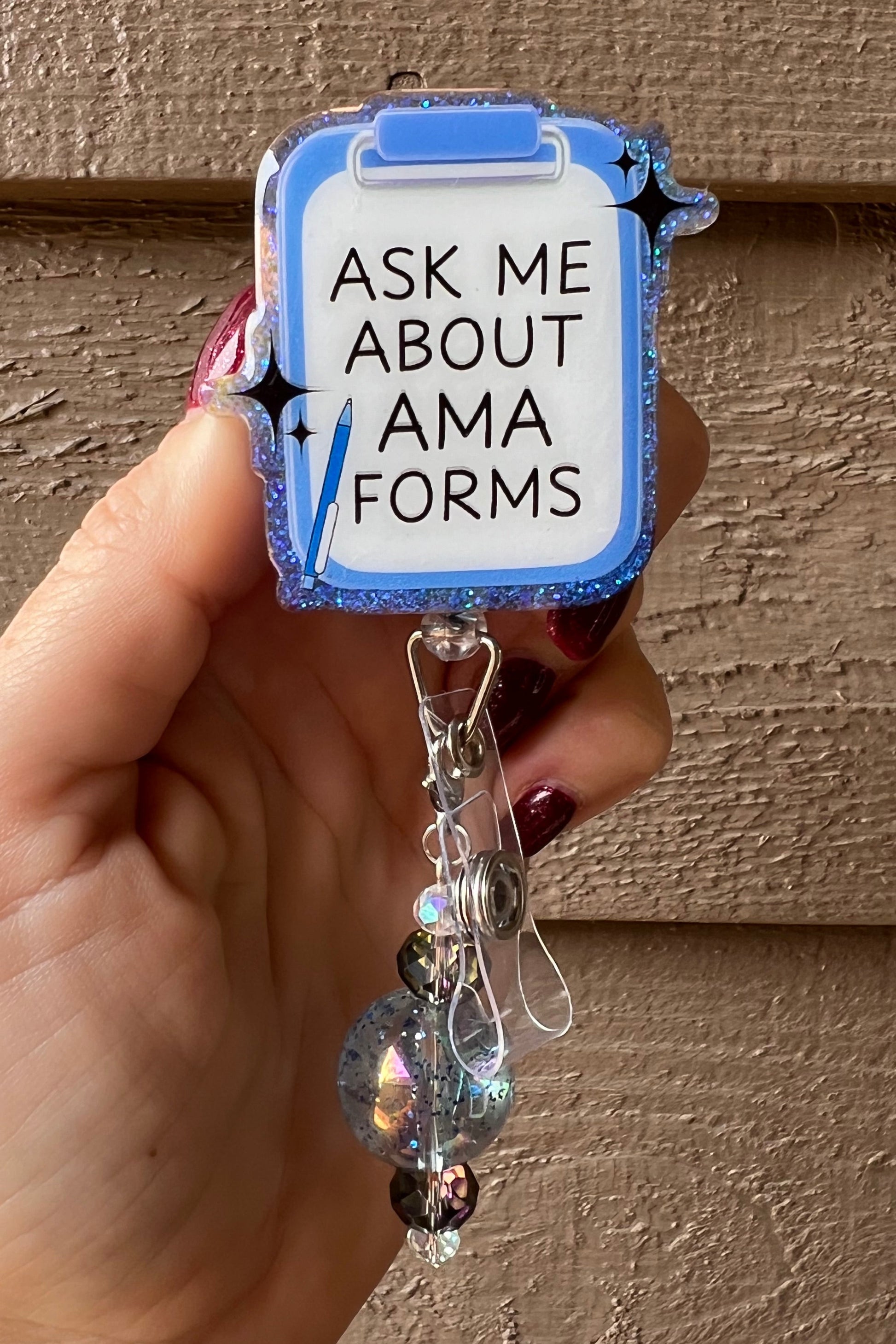 A glittery blue clipboard-shaped badge reel with the phrase “Ask Me About AMA Forms,” decorated with holographic and black beads. Perfect for medical professionals and healthcare workers.