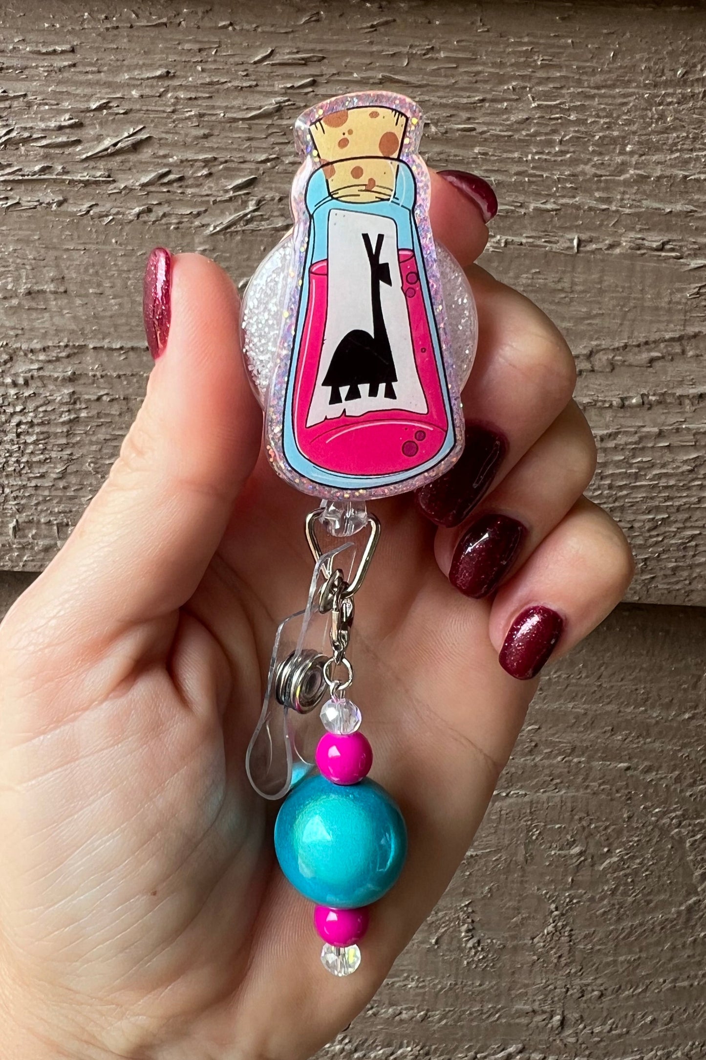 Badge Reel with glittery Kuzco potion bottle design and teal/pink beaded dangle.