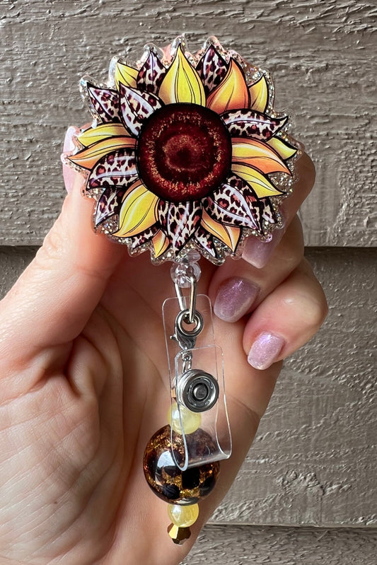 A yellow and brown sunflower with a leopard print design, glitter, and a clear plastic badge holder with a silver retractable clip.