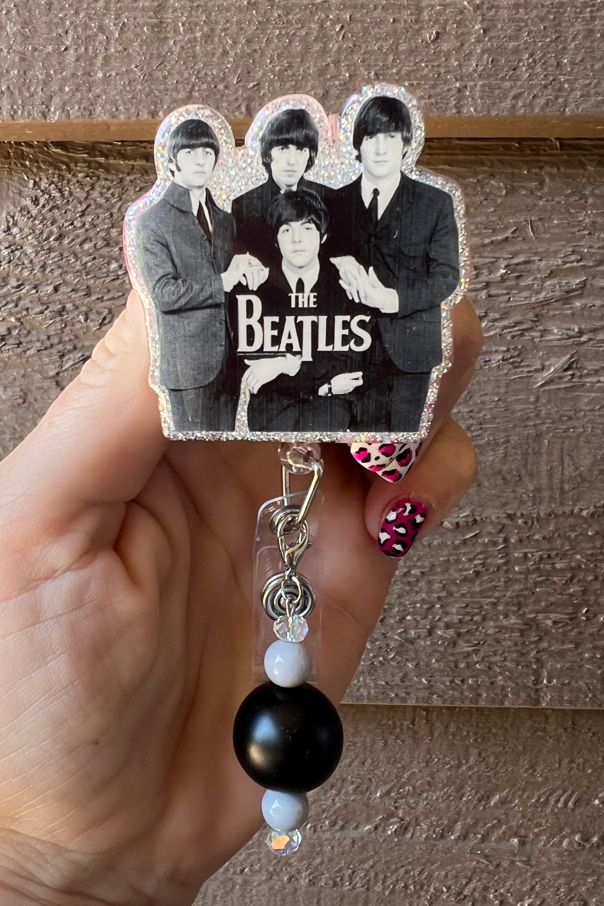 Hand holding badge reel featuring the iconic Rock and Roll band, The Beatles with coordinating badge bling.