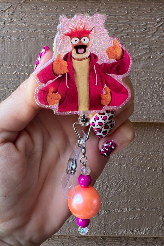 Pepe the King Prawn badge reel with glitter background and pink/orange beaded dangle, wearing a red hoodie