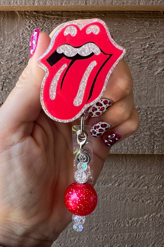 Hand holding Rolling Stones badge reel over soft white pearl glitter with coordinating badge bling.