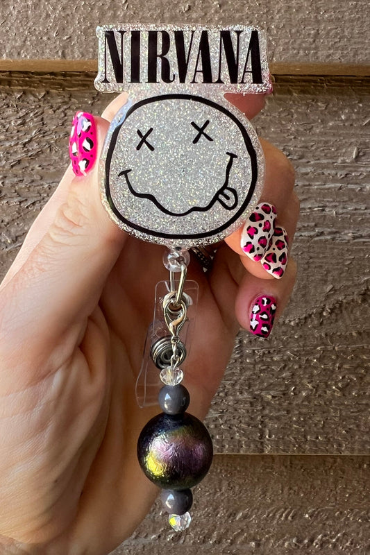 Hand holding Nirvana badge reel over holographic silver glitter with coordinating badge bling.