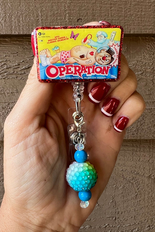 Hand holding classic Operation Game badge reel with red glitter border and coordinating badge bling.