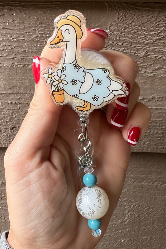 Hand holding porch duck badge reel in floral dress and hat with matching badge bling.