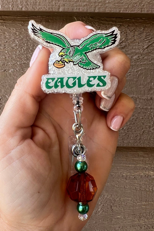 Pearl glitter Eagles badge reel with vintage design and green/amber beaded dangle.